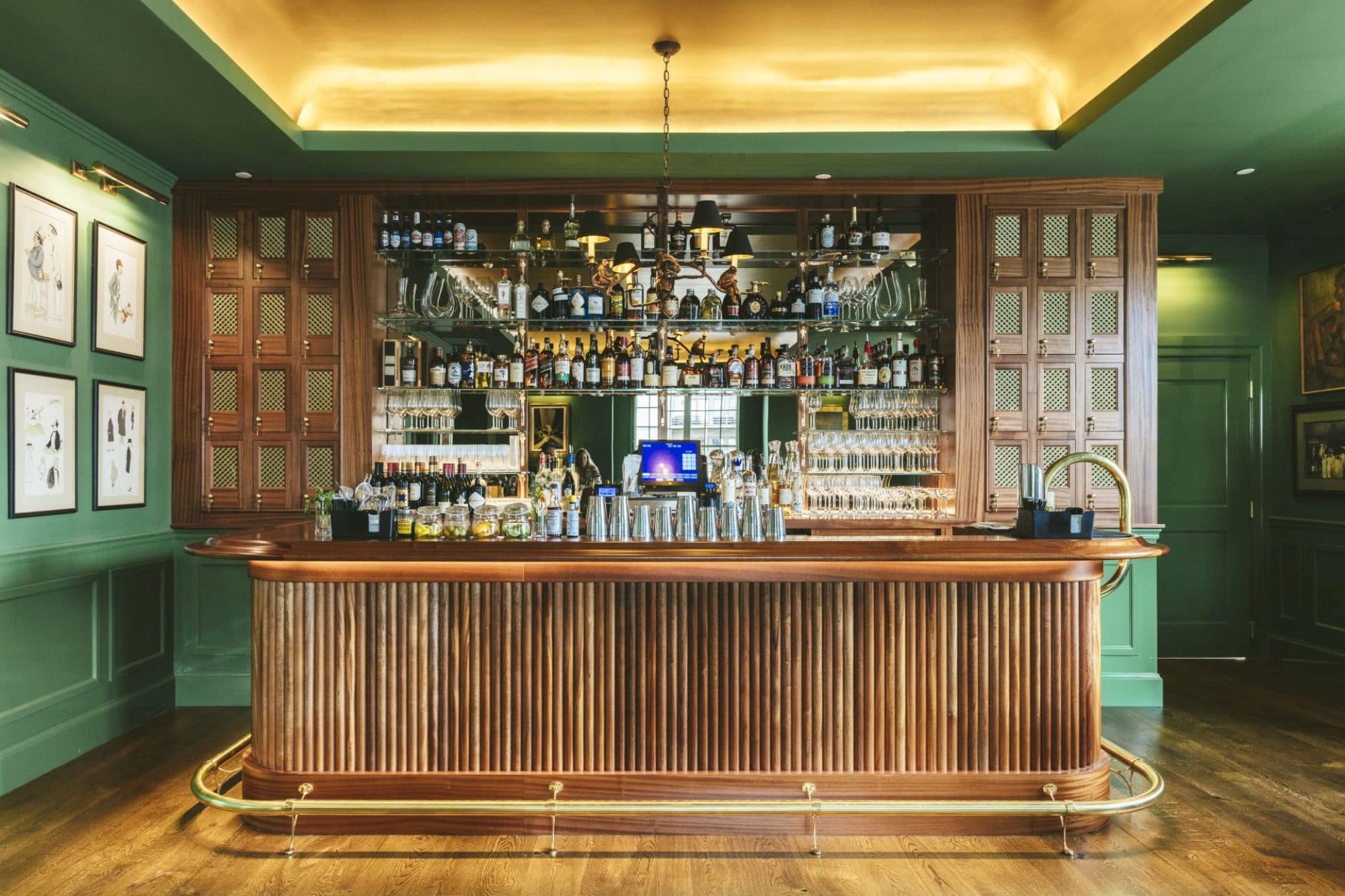 This image shows a well-stocked, stylish bar with a wooden counter, ornate shelving, various bottles, and dim lighting, creating a cozy atmosphere.