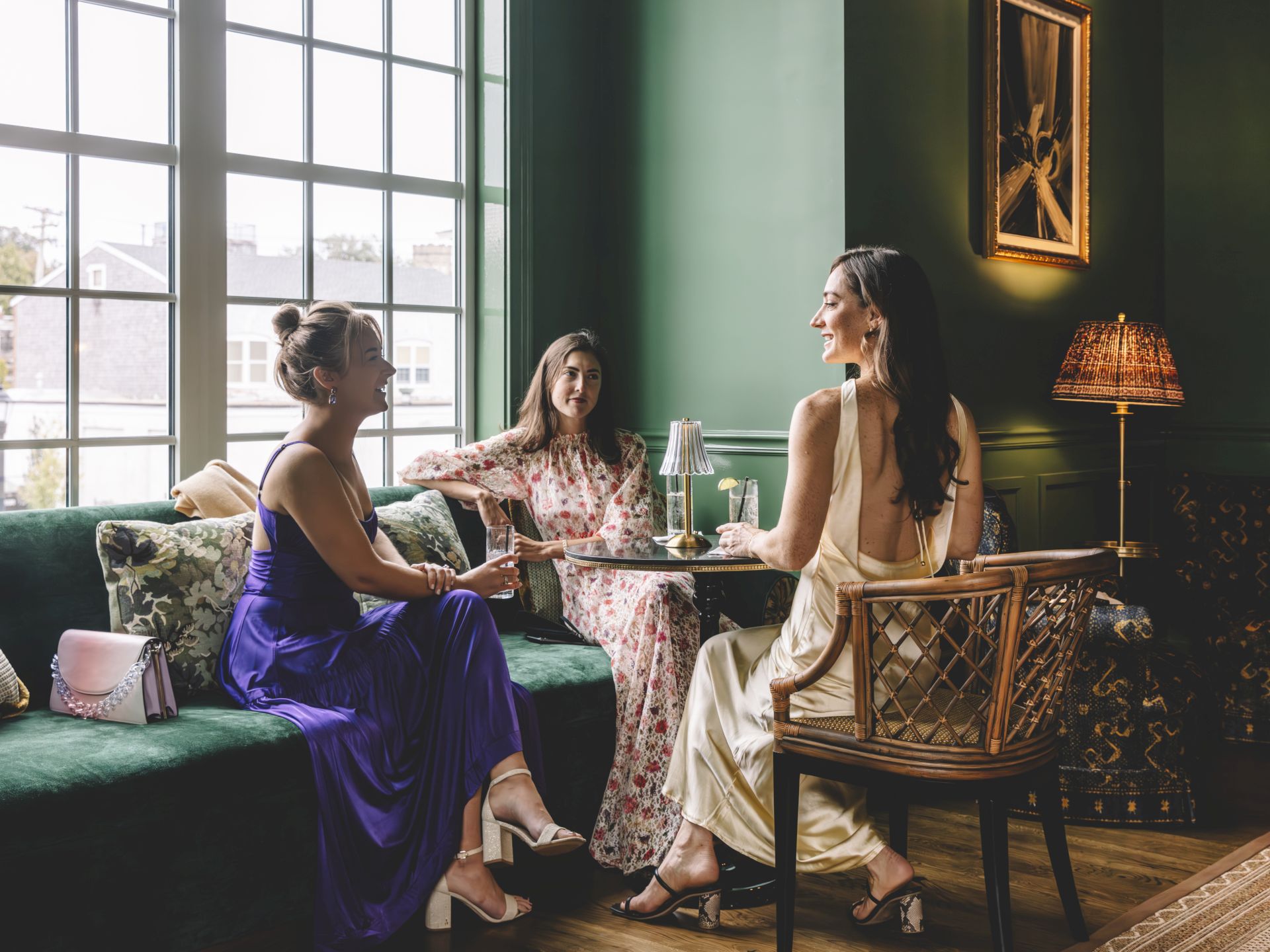 Three women in formal dresses sitting in a lounge with green walls and a green velvet couch.
