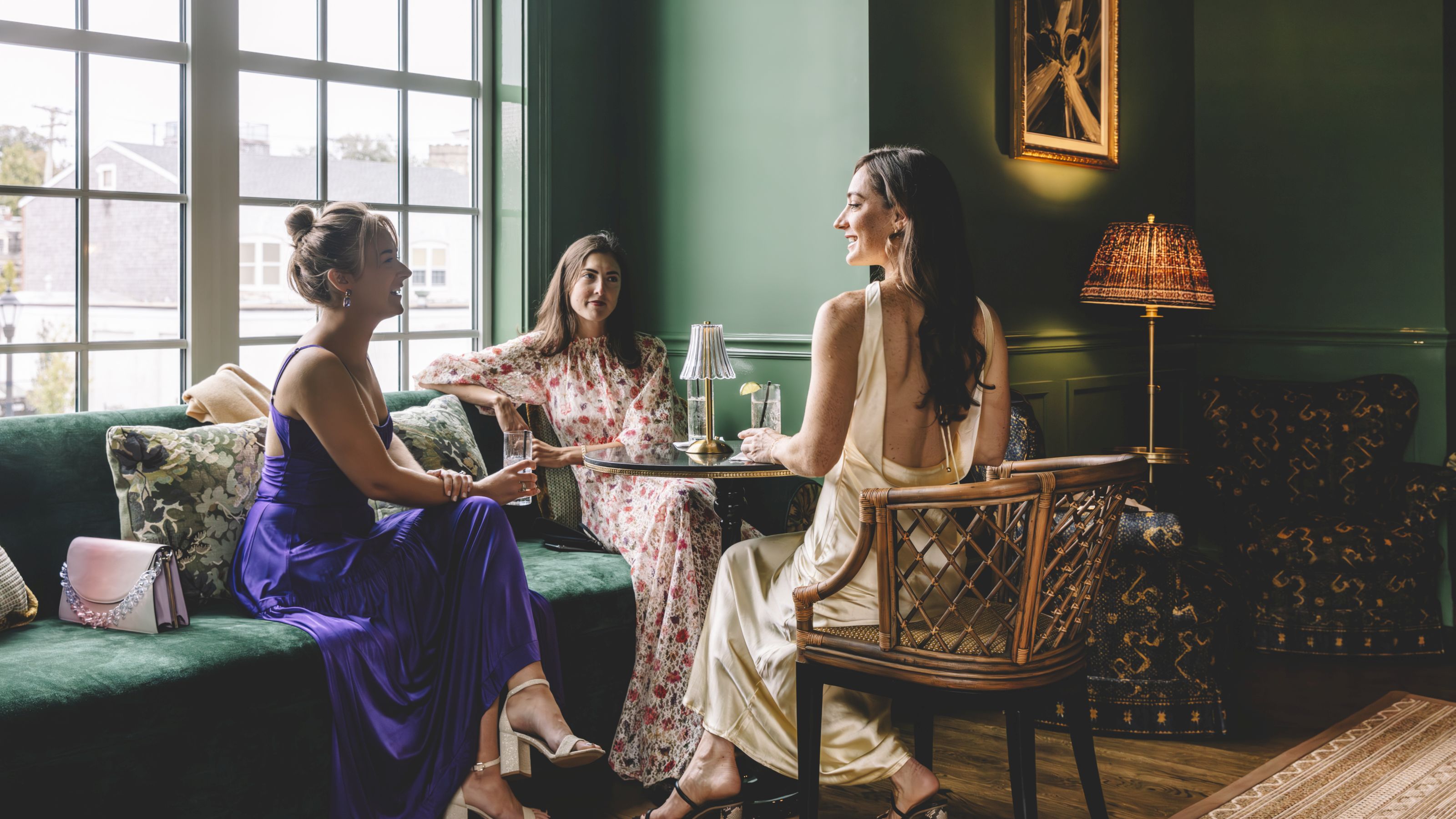 Three women sitting in a lobby lounge area with a green velvet sofa, wooden chair, and coffee table.