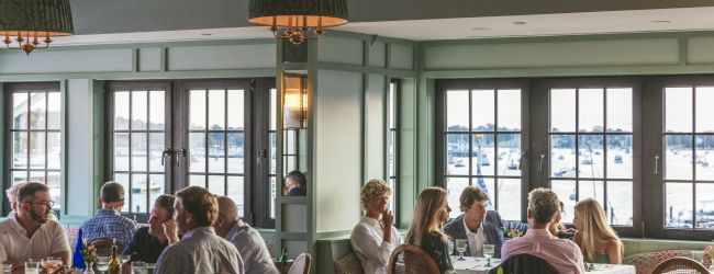 People dining in a cozy, elegantly decorated restaurant with large windows and a view of the water outside.