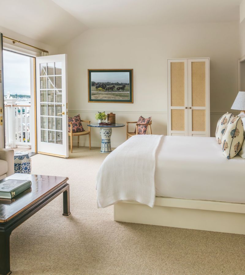 A wide-angle view of a hotel room with a large bed, a sitting area, and a balcony door leading outside.