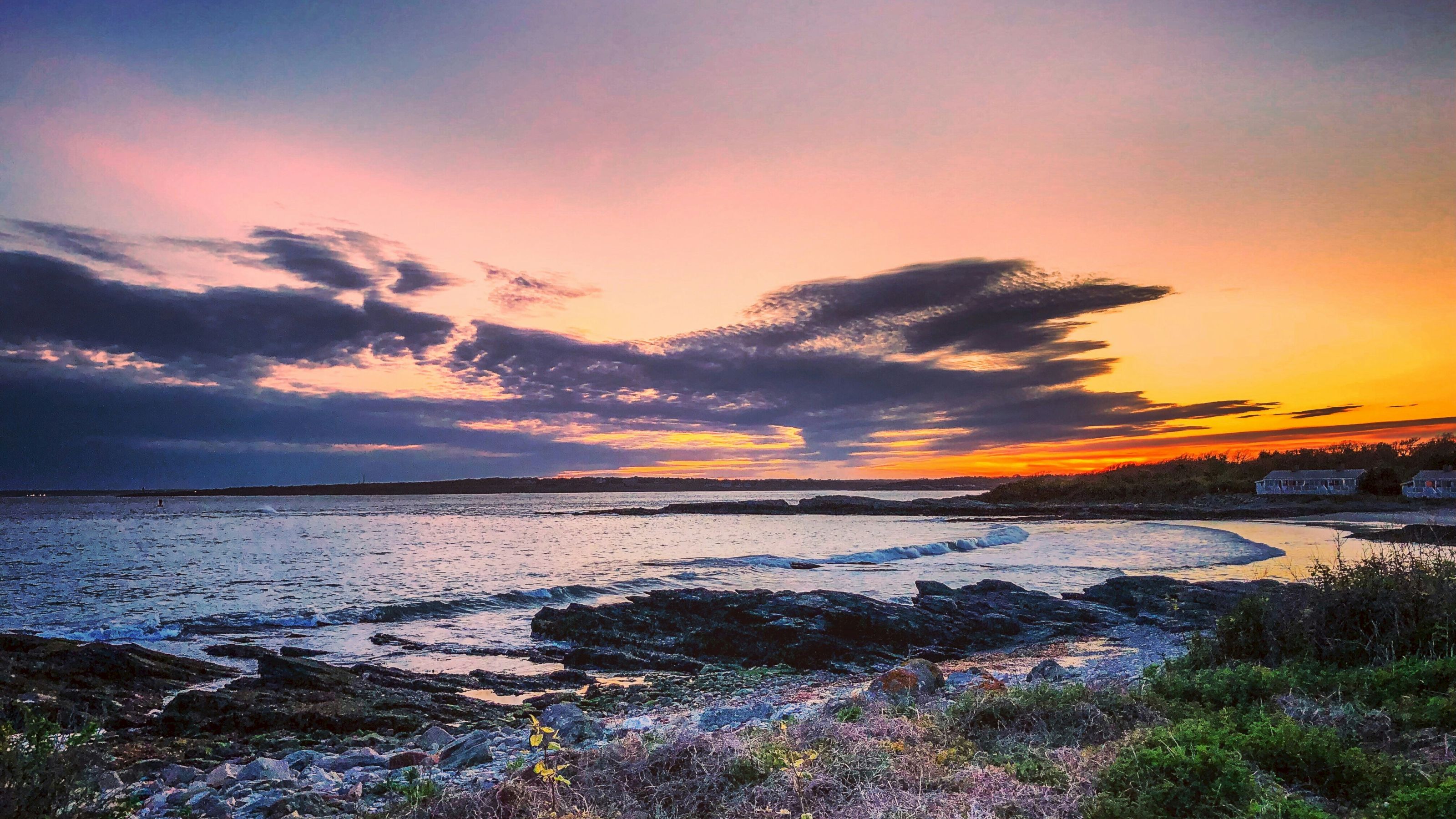 a sunset over a body of water with rocks in the foreground