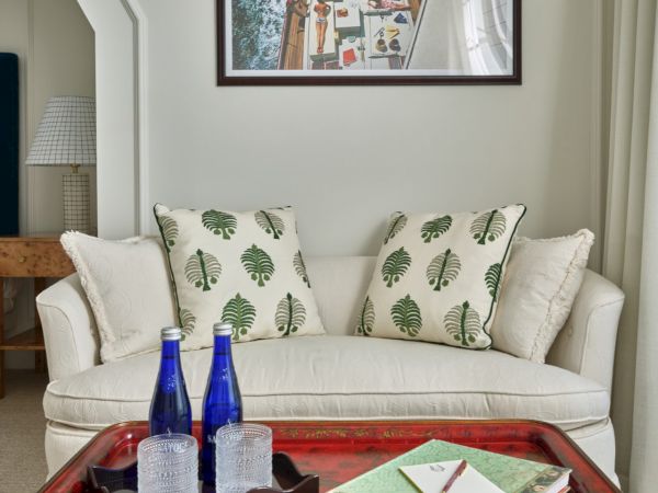 A cozy sitting area in a Newport, RI, hotel room with a sofa, leaf-themed pillows, and a table with a red tray and blue bottles.