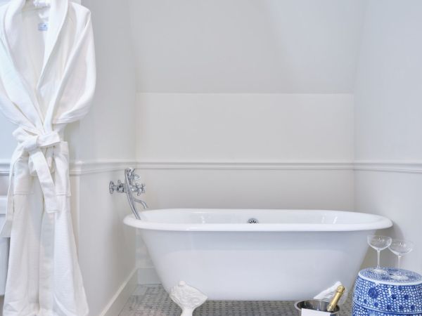 A bathroom with a white bathtub, a white bathrobe hanging, and a blue and white decorative stool in a Newport, RI, hotel room.
