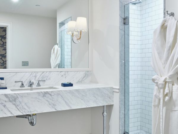A modern bathroom in a Newport, RI, hotel room with a marble countertop, large mirror, glass shower, and a white robe on the wall.