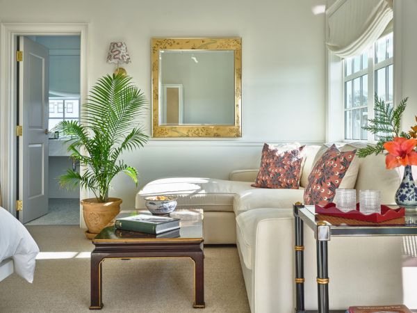 A cozy sitting area in a Newport, RI, hotel room with a large mirror, a coffee table, and a cream sofa with printed pillows.