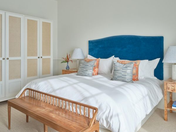 A cozy Newport, RI, hotel room with a large bed, wooden bench, bedside tables, lamps, and a wicker wardrobe.