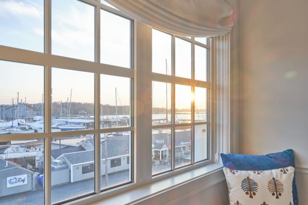 The image captures a serene view of a marina through a large window, with a cozy cushion placed on the windowsill, bathed in sunlight.