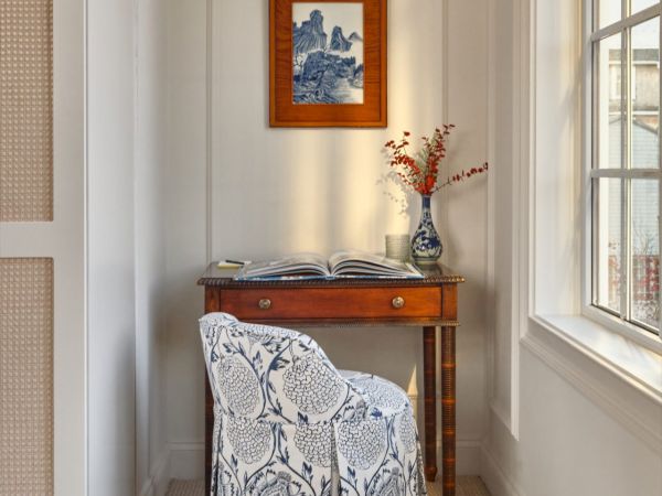 A desk setup in a Newport, RI, hotel room featuring a wooden desk, a floral upholstered chair, and a framed artwork on the wall.