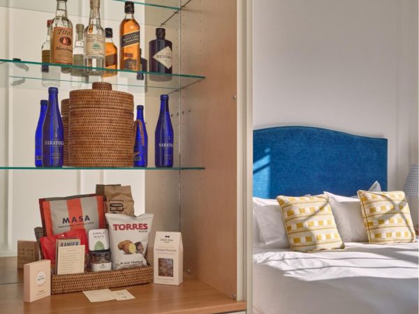 A close up on a cabinet holding bottles, glasses, and decor in a Newport, RI, hotel room. In the background is a large bed.