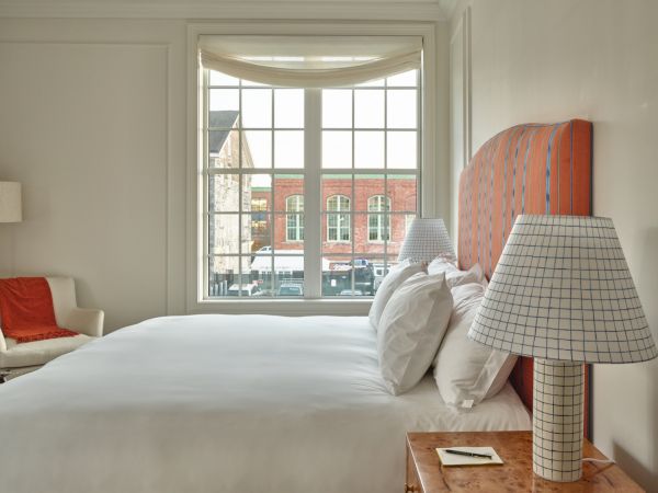 A well-lit Newport, RI, hotel room with a large window, featuring a large bed, lamps with checkered shades, and a cozy chair.