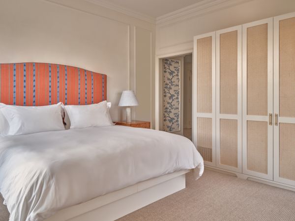 A bright Newport, RI, hotel room with a large bed, side tables, lamps, a window seat with cushions, and a scenic window view.
