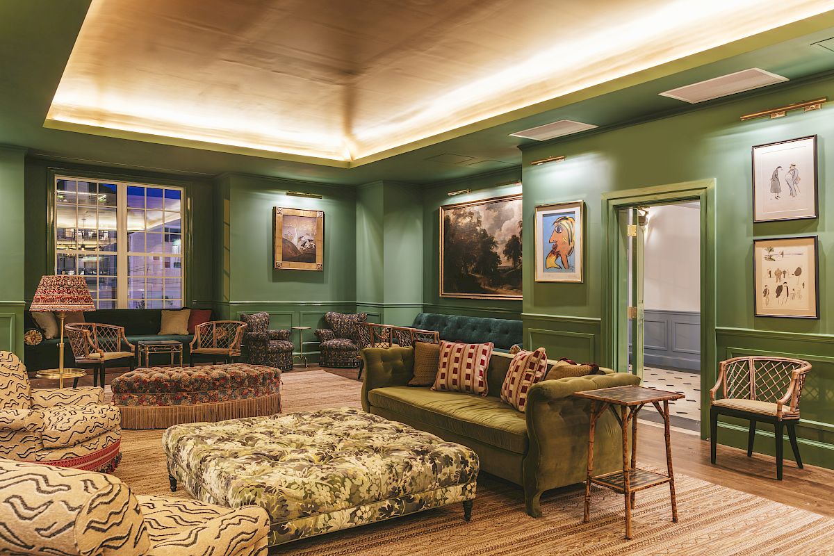 The Studio Bar decorated with green walls, wicker chairs, a plush coffee table, a green couch, framed art, and warm lighting.
