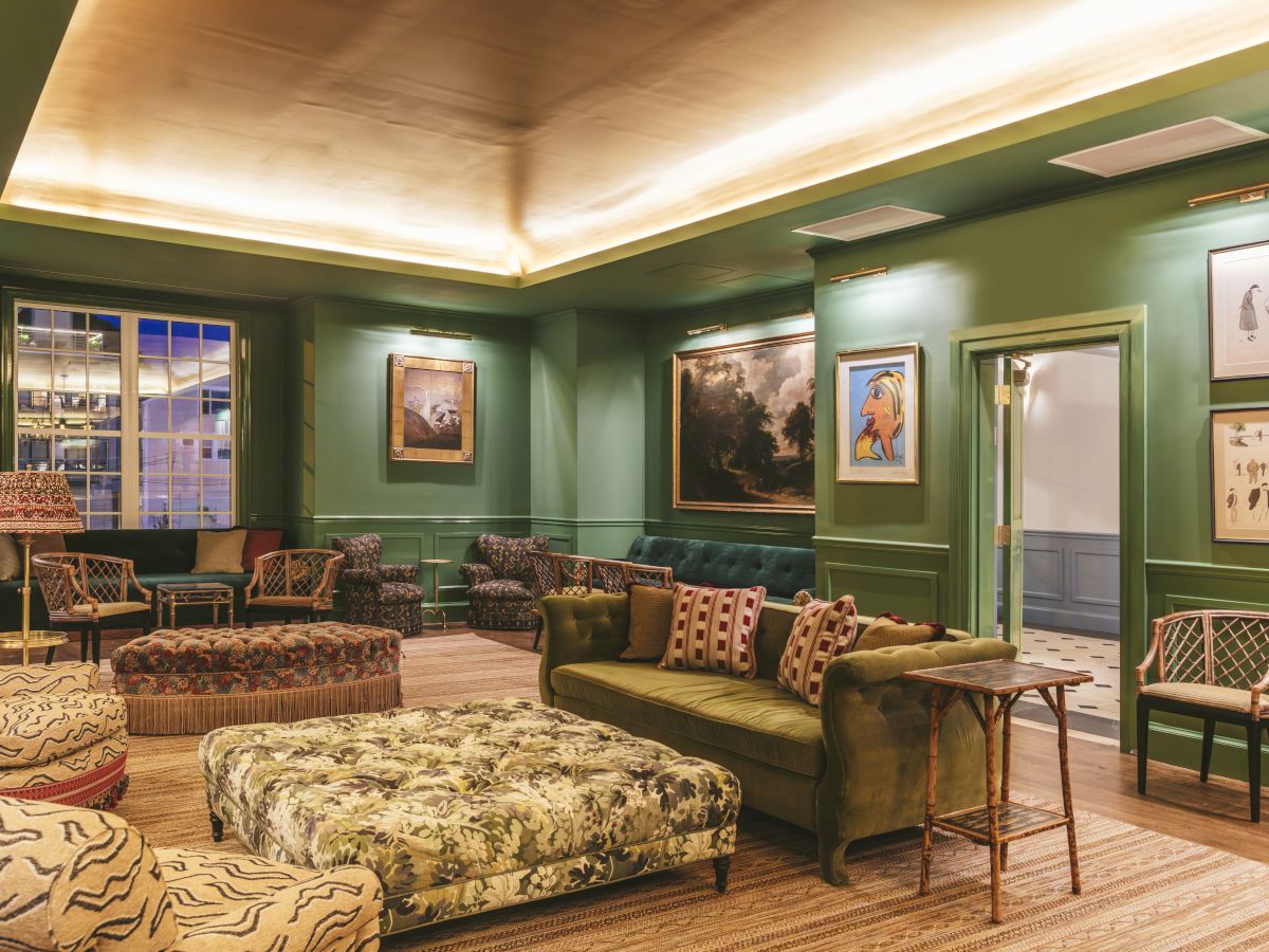 The Studio Bar decorated with green walls, wicker chairs, a plush coffee table, a green couch, framed art, and warm lighting.