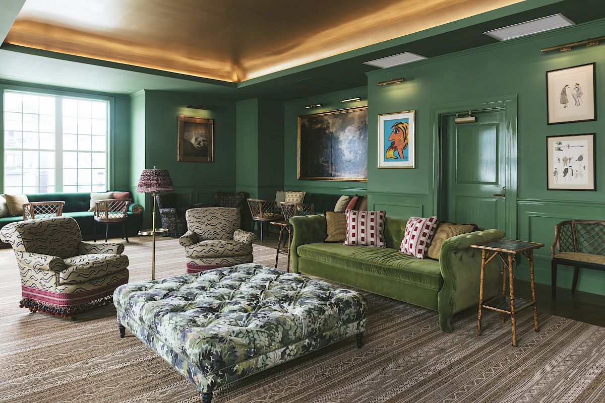 The Studio Bar decorated with green walls, artwork, booth seating, a large window, round tables, and wicker chairs.