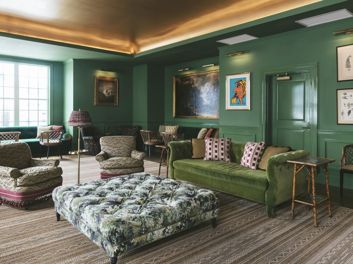 The Studio Bar decorated with green walls, artwork, booth seating, a large window, round tables, and wicker chairs.