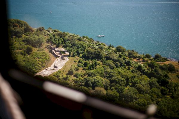 Aerial view of a lush, green landscape meeting a body of water, with a boat visible on the water.