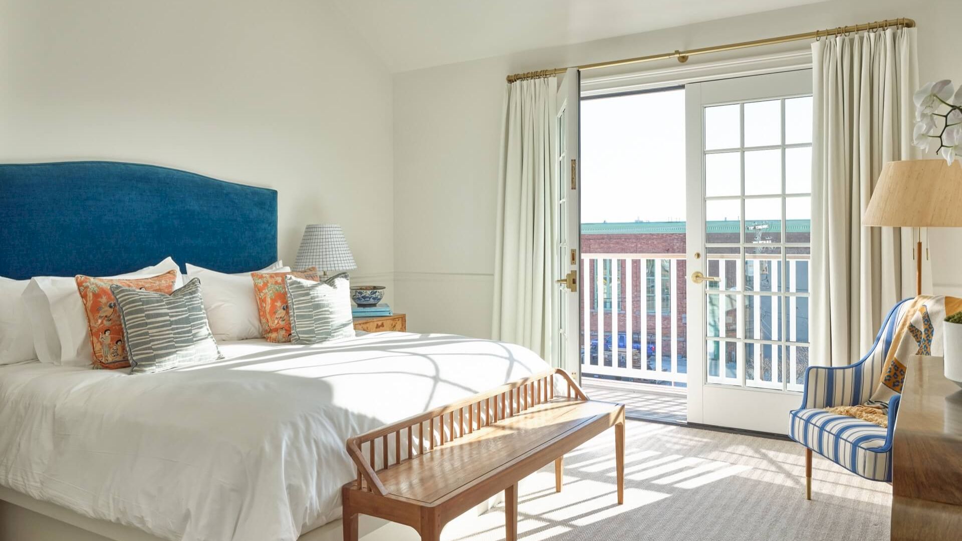 A bright and airy hotel room with a large bed, wooden bench, and blue accent chair.