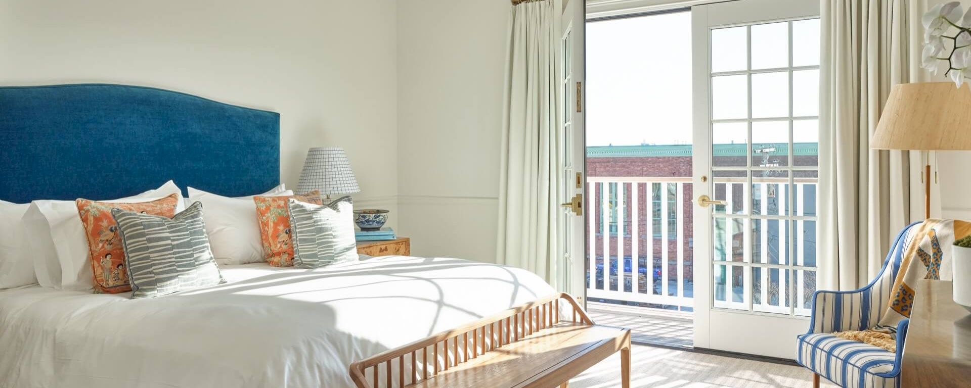 A hotel room with a bed, balcony, chair, and lamp.