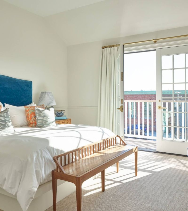 A bright and airy bedroom with a large bed, bench, and access to a balcony.