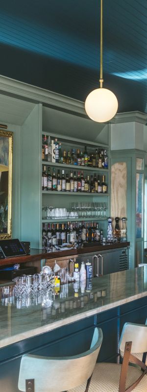 The image shows an upscale bar with a long marble counter, well-stocked shelves, modern pendant lights, and a mural on the back wall. The sentence ends.