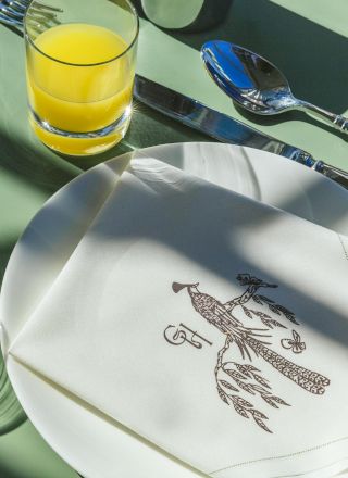 Two place settings with white plates, folded napkins with a bird design, orange juice, and silver cutlery on a green tablecloth.