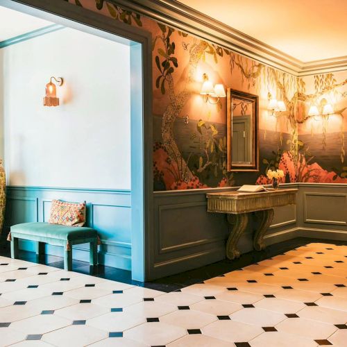 Elegant room with floral wallpaper, a large vase, a bench with cushions, and a decorative table beneath a mirror.