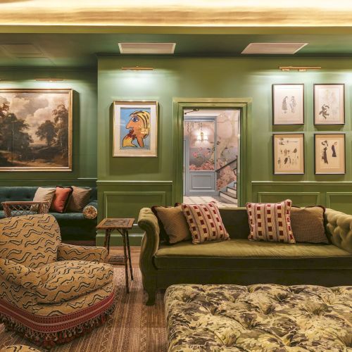 A stylish green room with sofas, armchairs, paintings, and framed art on the walls, creating an elegant and cozy atmosphere.