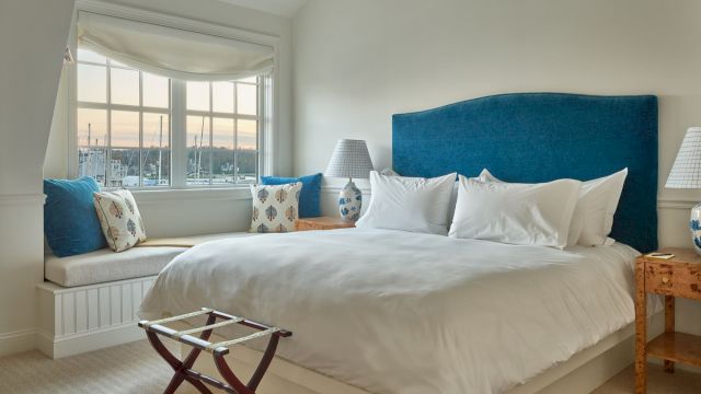 A hotel room with a blue headboard, white bedding, and a window seat.