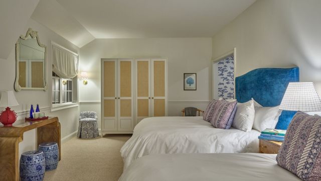 A wide view of a hotel room with two beds, a blue headboard, and a wooden console table.