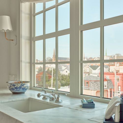 A bright kitchen features a large window, sink, faucet, decorative bowl, and cityscape view, creating a fresh, open atmosphere.