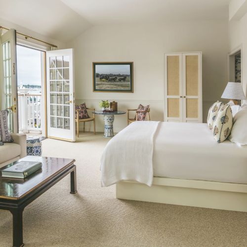 A bright, cozy bedroom with a bed, sofa, coffee table, and balcony access. Decor is minimal, with paintings and patterned cushions.