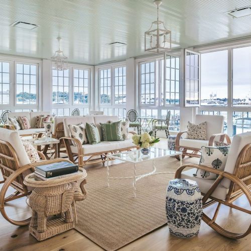 A bright, airy room with wicker furniture, large windows, and nautical-themed decor, offering a cozy sitting area with natural light.