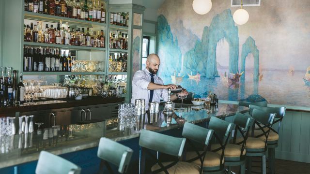 a bartender stands behind a bar with shelves of liquor and glasses