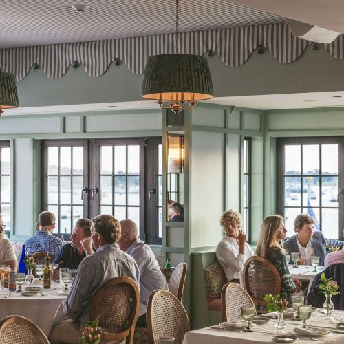 A group of people dining in a cozy restaurant with large windows showing a view of boats on the water.