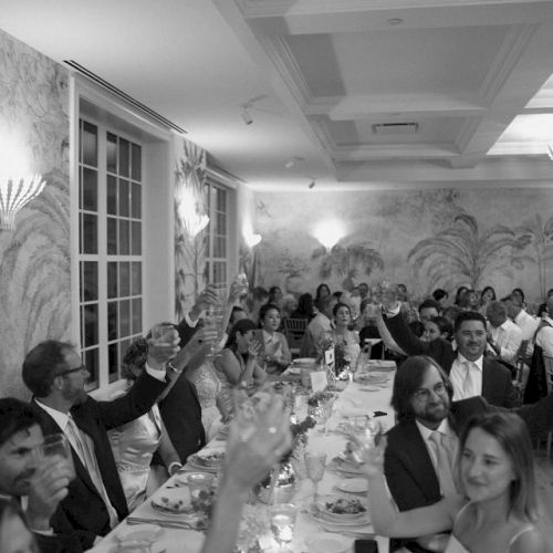 A black-and-white photo of a formal dinner event, with people seated at long tables, raising glasses in a toast.