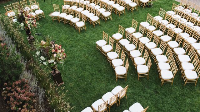 An outdoor event setup with rows of chairs and floral arrangements on a grassy area.